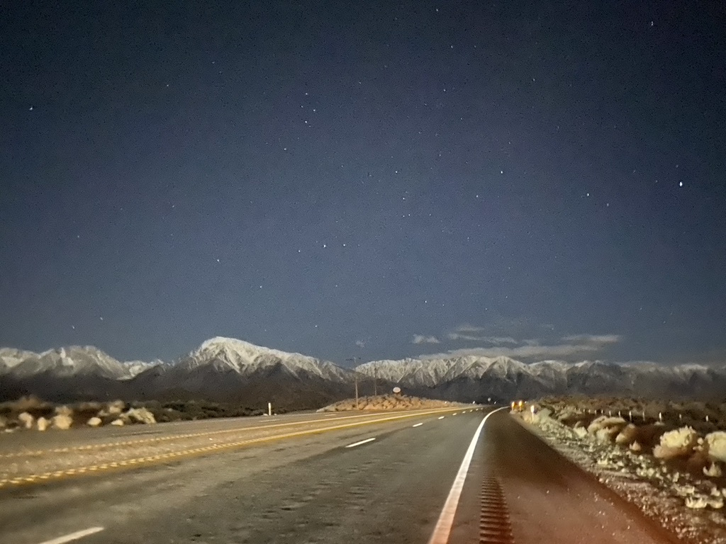 A clear starry winter night on a road bordered by snow capped Sierra Nevada in California