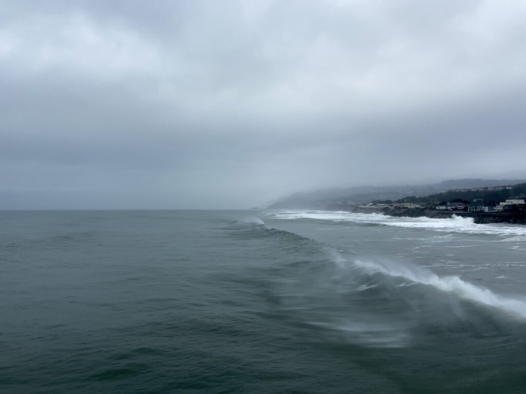Pacific waves spray mist and crash on the and California coast under grey winter skies